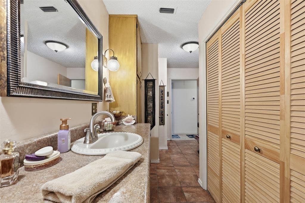 777 Wildwood Trail, Weatherford, TX 76085 Bathroom vanity featuring a decorative framed mirror, wall-mounted sconce lighting, and a neutral-toned countertop with an integrated sink