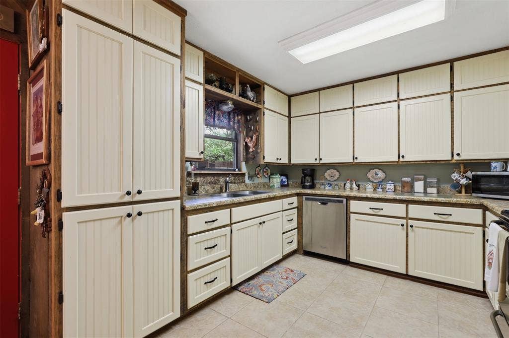 777 Wildwood Trail, Weatherford, TX 76085 Kitchen featuring extensive beadboard cabinetry with contrasting wood-finish trim, a double basin stainless steel sink, and light-toned tile flooring
