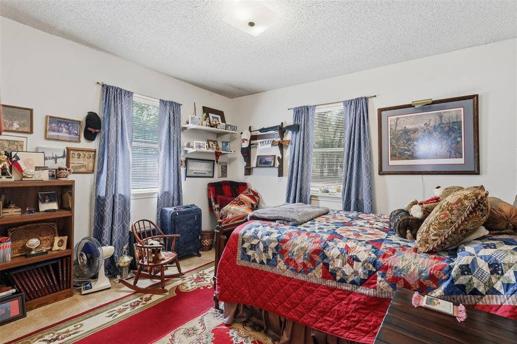 777 Wildwood Trail, Weatherford, TX 76085 Bright room featuring two windows with horizontal blinds and blue patterned drapes, a ceiling-mounted light fixture, and textured ceilings