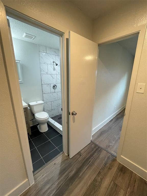 822 Johnnie Row, Seagoville, TX 75159 Bathroom featuring vanity, a textured ceiling, a tile shower, hardwood / wood-style flooring, and toilet