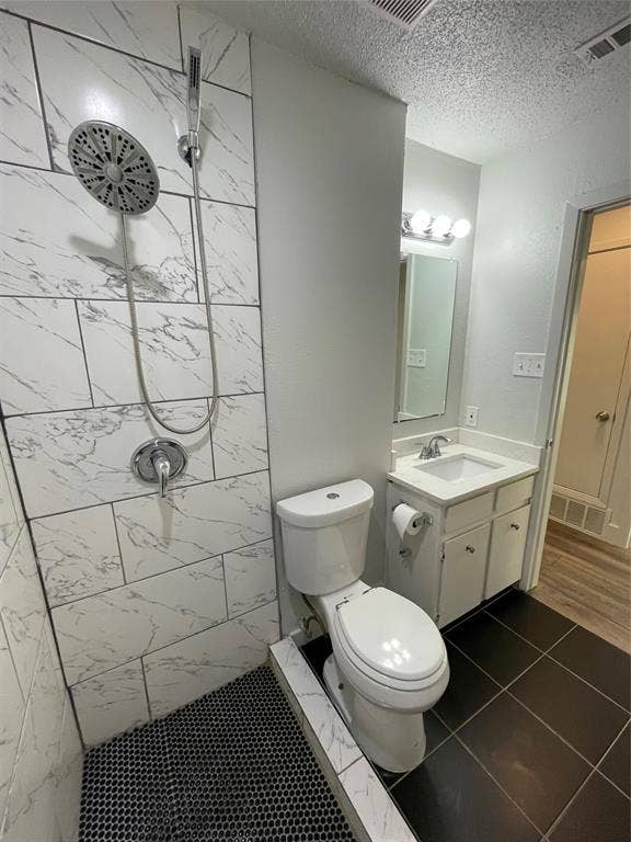 822 Johnnie Row, Seagoville, TX 75159 Bathroom featuring tiled shower, vanity, a textured ceiling, tile patterned flooring, and toilet