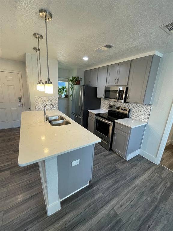822 Johnnie Row, Seagoville, TX 75159 Kitchen featuring dark wood-type flooring, backsplash, stainless steel appliances, decorative light fixtures, and sink