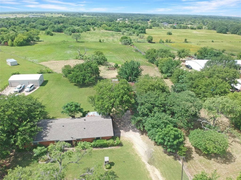 8769 S Fm 148, Scurry, TX 75158 Sprawling property featuring a ranch-style home with a gray shingle roof, surrounded by mature trees and expansive green fields