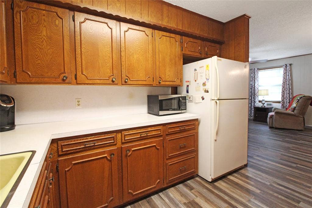 8769 S Fm 148, Scurry, TX 75158 Kitchen featuring wood cabinetry, white countertops, a built-in refrigerator alcove, and wood-finish flooring extending into the adjacent living space