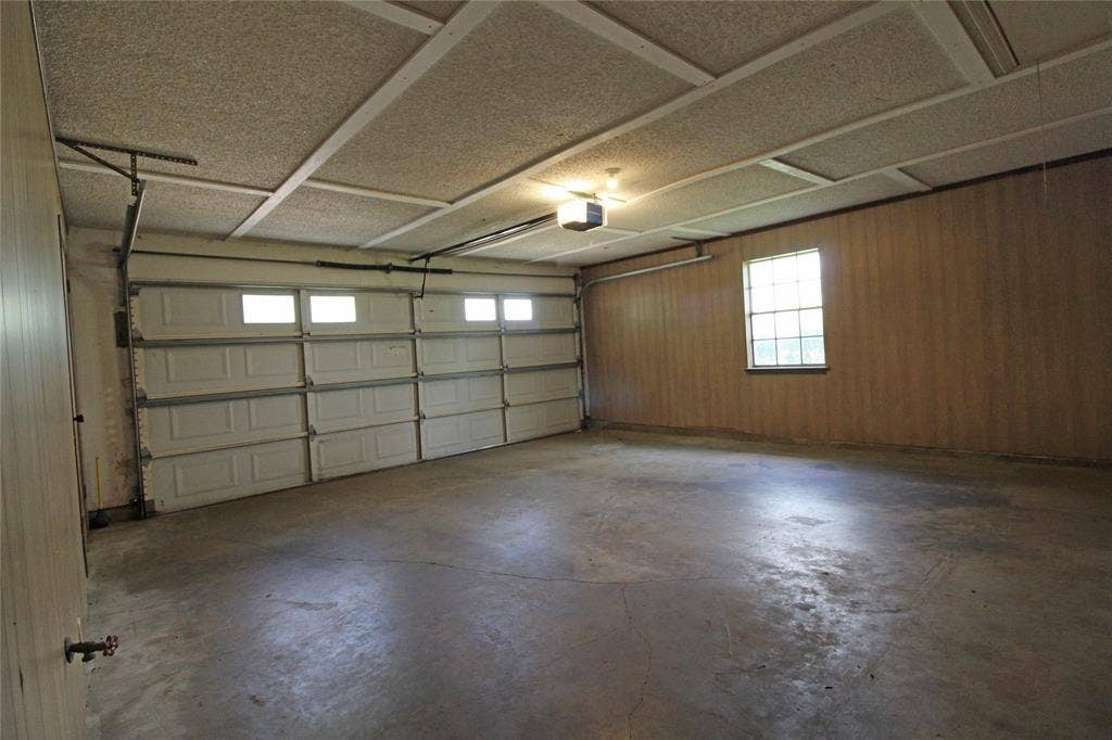 8769 S Fm 148, Scurry, TX 75158 Spacious garage featuring a concrete floor, two white paneled garage doors with upper windows, wood-paneled walls, a window with grilles, and a drop ceiling with acoustic panels