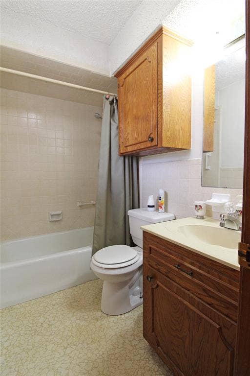 8769 S Fm 148, Scurry, TX 75158 Bathroom featuring a built-in bathtub with tiled surround, a white toilet, and a vanity with wood-finish cabinetry and a light-colored countertop with an integrated sink
