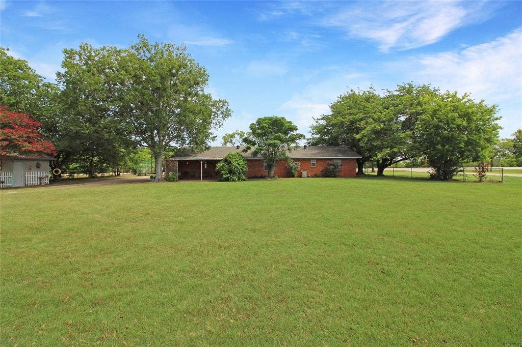 8769 S Fm 148, Scurry, TX 75158 Expansive green lawn with mature trees and a brick-sided residence