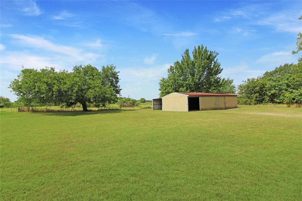 8769 S Fm 148, Scurry, TX 75158 Expansive green lawn featuring a metal outbuilding with open bays, mature trees, and perimeter fencing