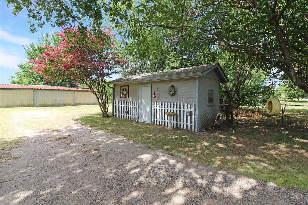 8769 S Fm 148, Scurry, TX 75158 Detached outbuilding with a gabled roofline, white picket fence, and a flowering tree