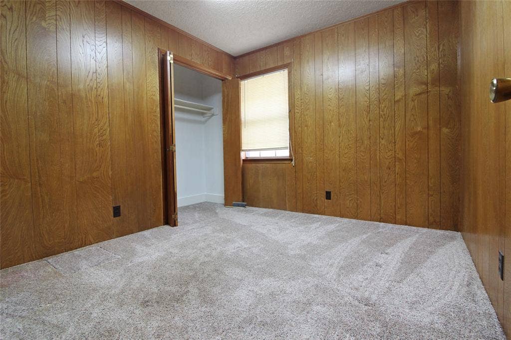 8769 S Fm 148, Scurry, TX 75158 Room featuring wood-paneled walls, light-toned carpet flooring, a window with a roller shade, and a closet with shelving
