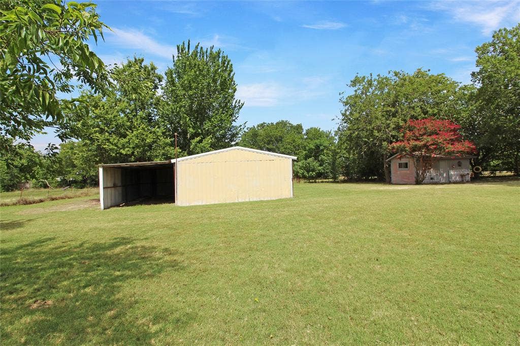 8769 S Fm 148, Scurry, TX 75158 Expansive grassy yard featuring a large open-sided metal utility building and a separate storage shed with a vibrant red-leafed tree