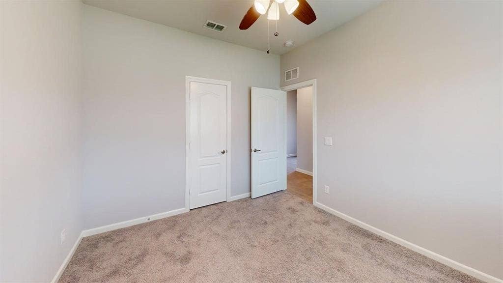 Room featuring neutral gray walls, plush carpet flooring, a ceiling fan with wood-finish blades, and white interior doors with curved paneling