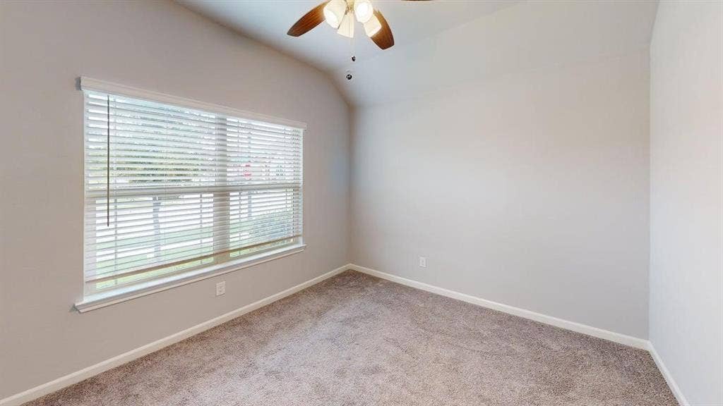 Carpeted interior space featuring a large window with white horizontal blinds, neutral wall paint, white baseboards, and a ceiling fan with integrated lighting