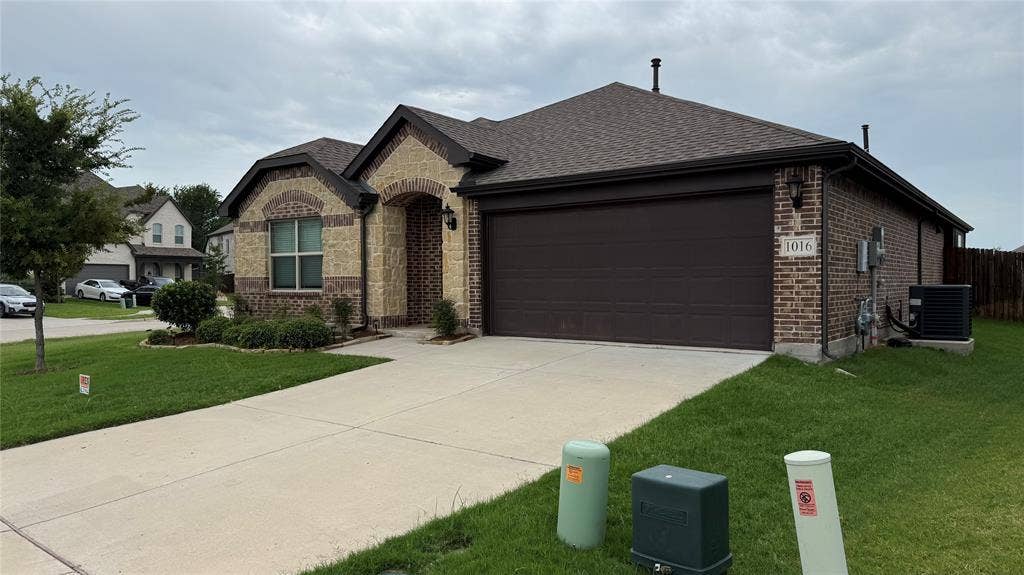 Brick and stone-veneer exterior featuring a brown garage door, arched entryway, and a gabled roof