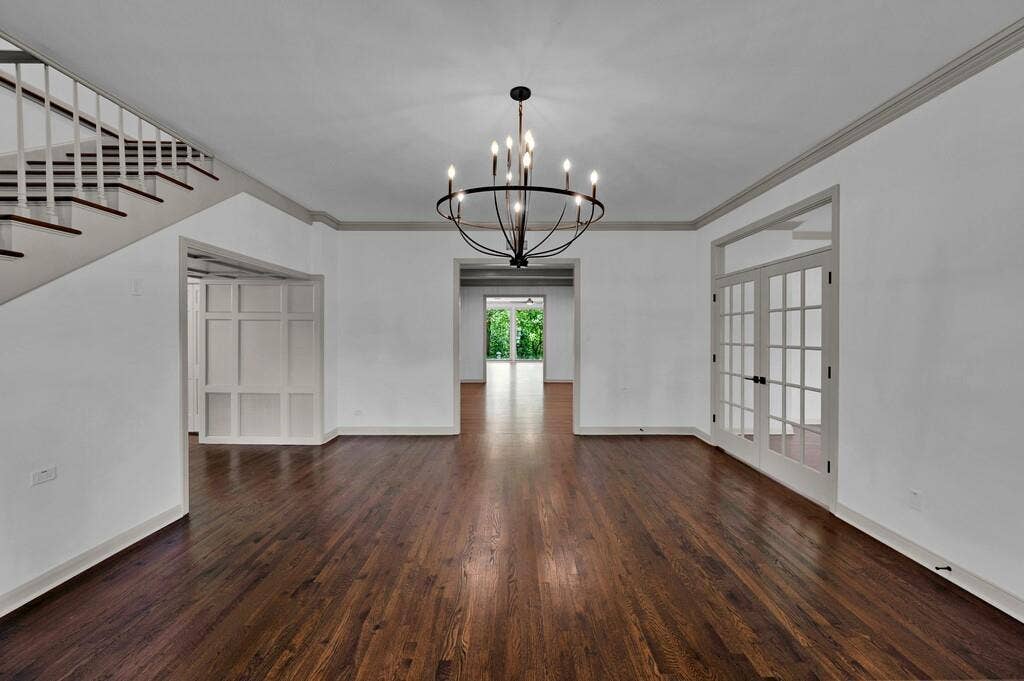 2825 Lake Air Drive, Waco, TX 76710 Spacious room featuring rich wood-finish flooring, a contemporary black metal chandelier, white walls with gray crown molding, and a staircase with white risers and dark wood treads