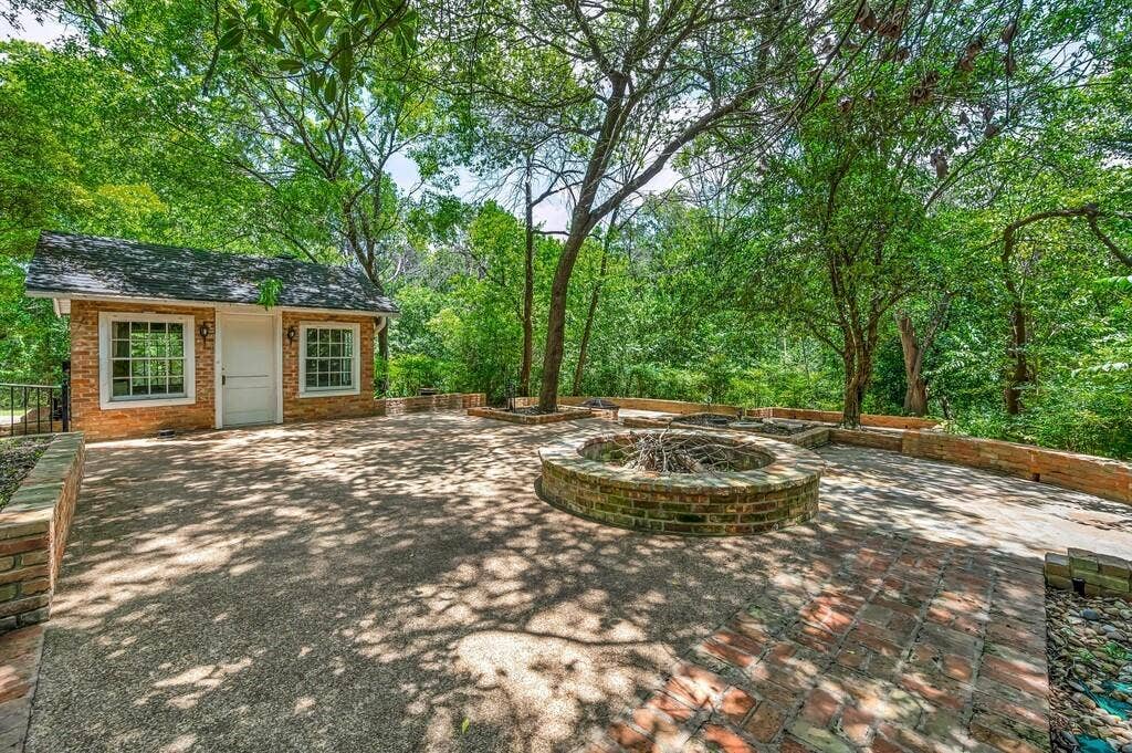 2825 Lake Air Drive, Waco, TX 76710 Expansive outdoor patio area featuring a built-in brick fire pit, a dedicated brick outbuilding, and mature trees providing natural canopy