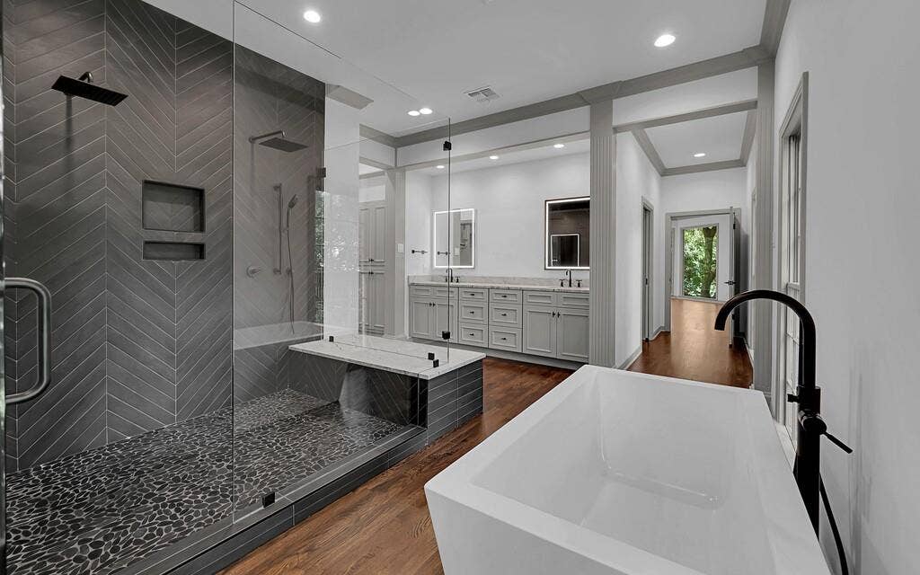 2825 Lake Air Drive, Waco, TX 76710 Modern bathroom featuring a freestanding soaking tub with a matte black floor-mounted faucet, a spacious glass-enclosed shower with dark chevron-patterned tile, and a dual vanity with light gray cabinetry and integrated sinks
