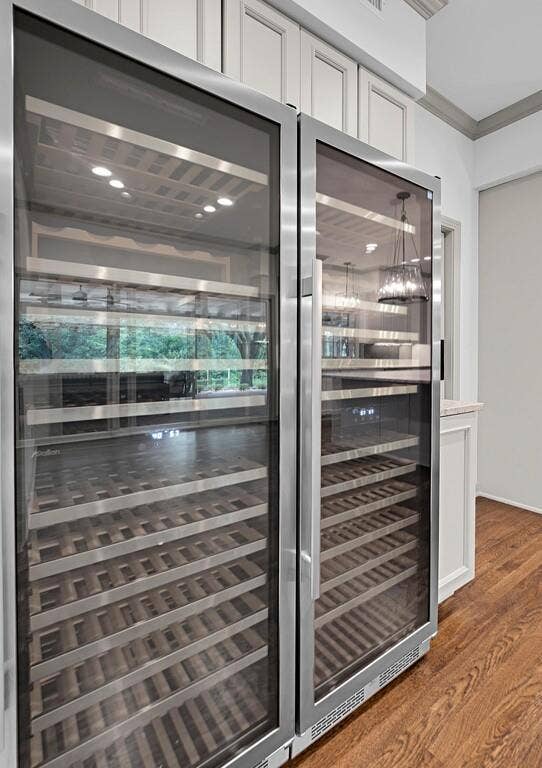 2825 Lake Air Drive, Waco, TX 76710 Integrated dual-zone wine refrigeration system with glass doors and wood-finish shelving, set within custom cabinetry featuring paneled doors, crown molding, and wood-finish flooring
