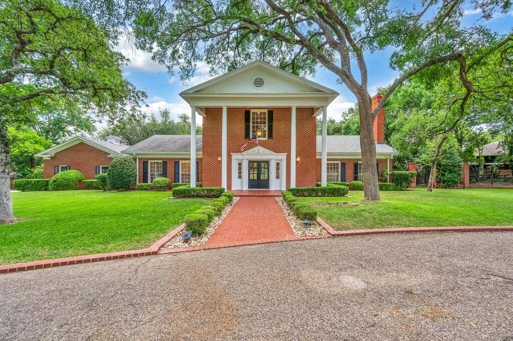 2825 Lake Air Drive, Waco, TX 76710 Classical brick residence featuring a prominent columned portico, a black double-entry door, and a red brick pathway