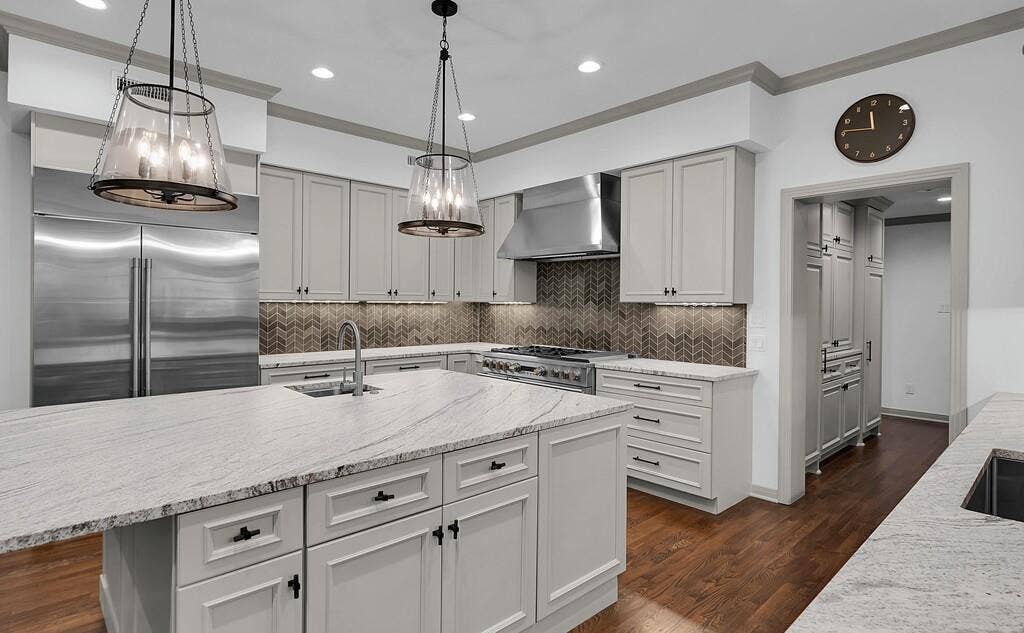2825 Lake Air Drive, Waco, TX 76710 Gourmet kitchen featuring a large central island with an undermount sink, stainless steel appliances, light-toned cabinetry with dark hardware, a herringbone pattern backsplash, and wood-finish flooring