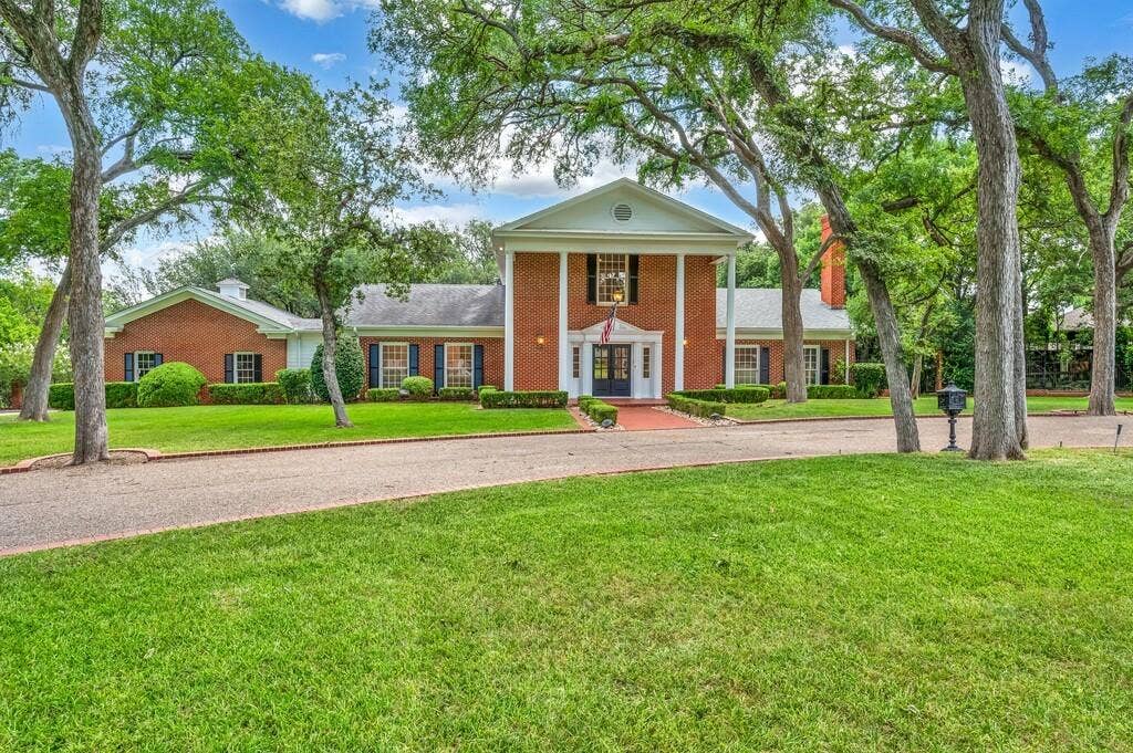 2825 Lake Air Drive, Waco, TX 76710 Brick colonial-style residence featuring a prominent columned portico and a gravel driveway