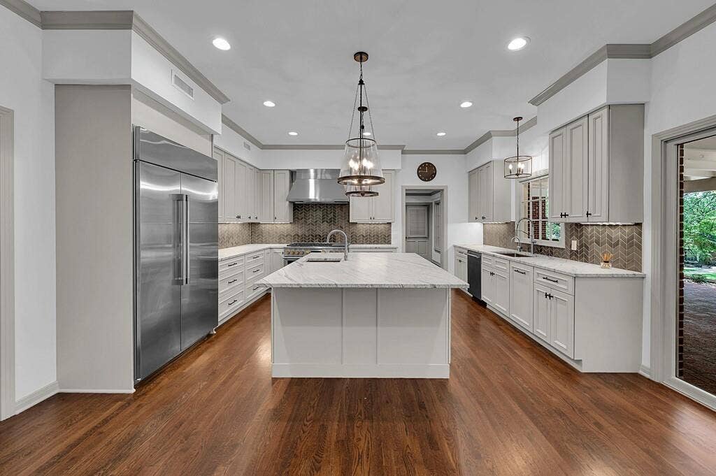 2825 Lake Air Drive, Waco, TX 76710 Spacious kitchen featuring a central island with a light-toned countertop, stainless steel appliances, light-toned cabinetry, a herringbone pattern backsplash, and wood-finish flooring