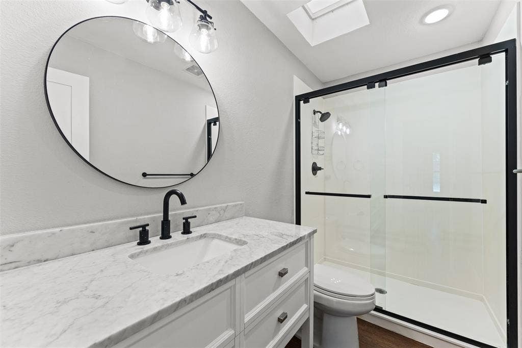 1405 Speight Avenue, #1, Waco, TX 76706 Bathroom featuring a white vanity with a stone countertop, a round frameless mirror, matte black fixtures, and a glass-enclosed shower with a black frame