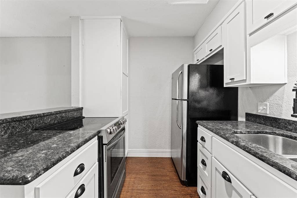 1405 Speight Avenue, #1, Waco, TX 76706 Galley kitchen featuring dark granite countertops, white cabinetry with dark hardware, stainless steel appliances, and wood-finish flooring