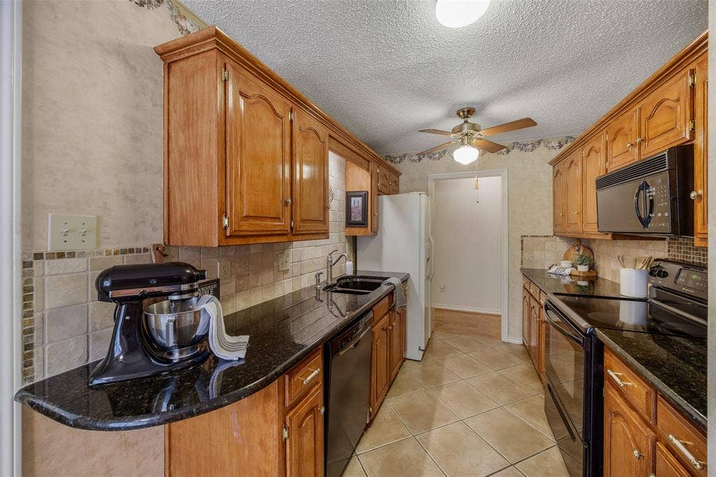 205 Covey Lane, McKinney, TX 75071 Galley kitchen featuring wood cabinetry, dark countertops, a tile backsplash, and tile flooring