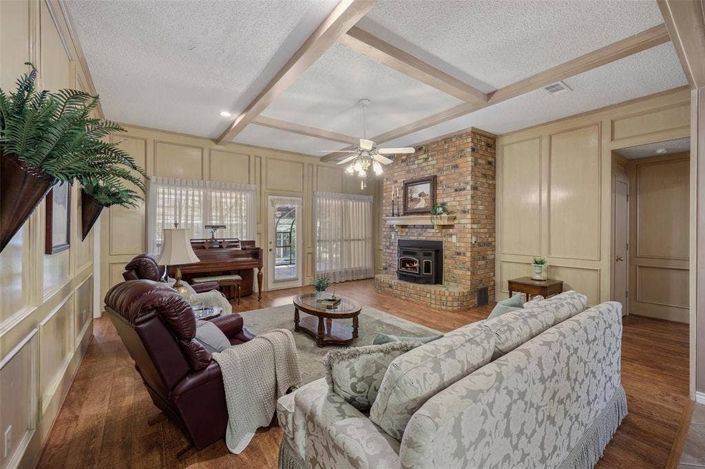 205 Covey Lane, McKinney, TX 75071 Spacious living area featuring wood-finish flooring, a brick fireplace with a mantel, and decorative paneling on the walls
