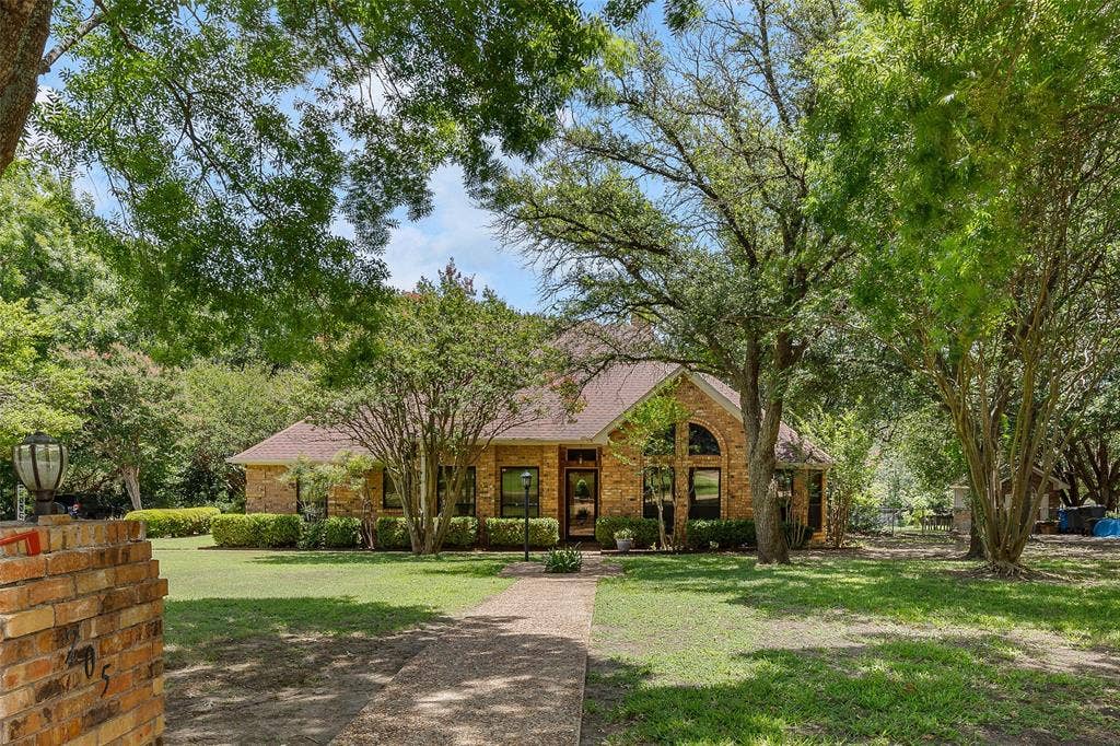 205 Covey Lane, McKinney, TX 75071 Brick exterior residence with a prominent arched window, mature trees, manicured shrubs, a concrete pathway, and a brick mailbox with an integrated lantern