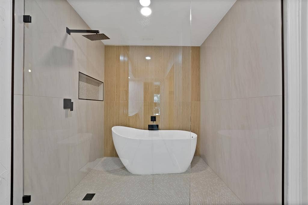 4021 San Mateo Drive, Plano, TX 75093 Walk-in shower enclosure with a freestanding soaking tub, matte black fixtures, integrated wall niche, and large format wall tiling