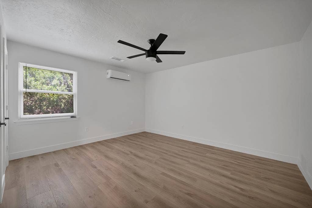 4021 San Mateo Drive, Plano, TX 75093 Spacious room featuring wood-finish flooring, a contemporary ceiling fan, and an individual wall-mounted climate control unit