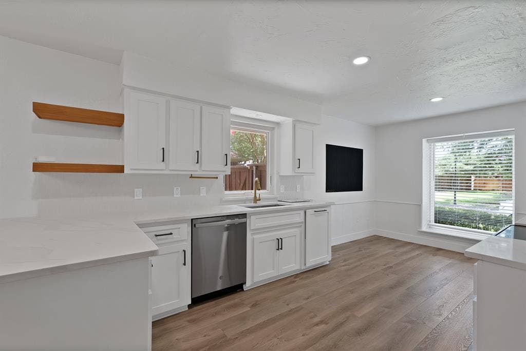 4021 San Mateo Drive, Plano, TX 75093 Kitchen featuring white shaker cabinetry with black hardware, light-toned countertops, a stainless steel dishwasher, and wood-finish flooring