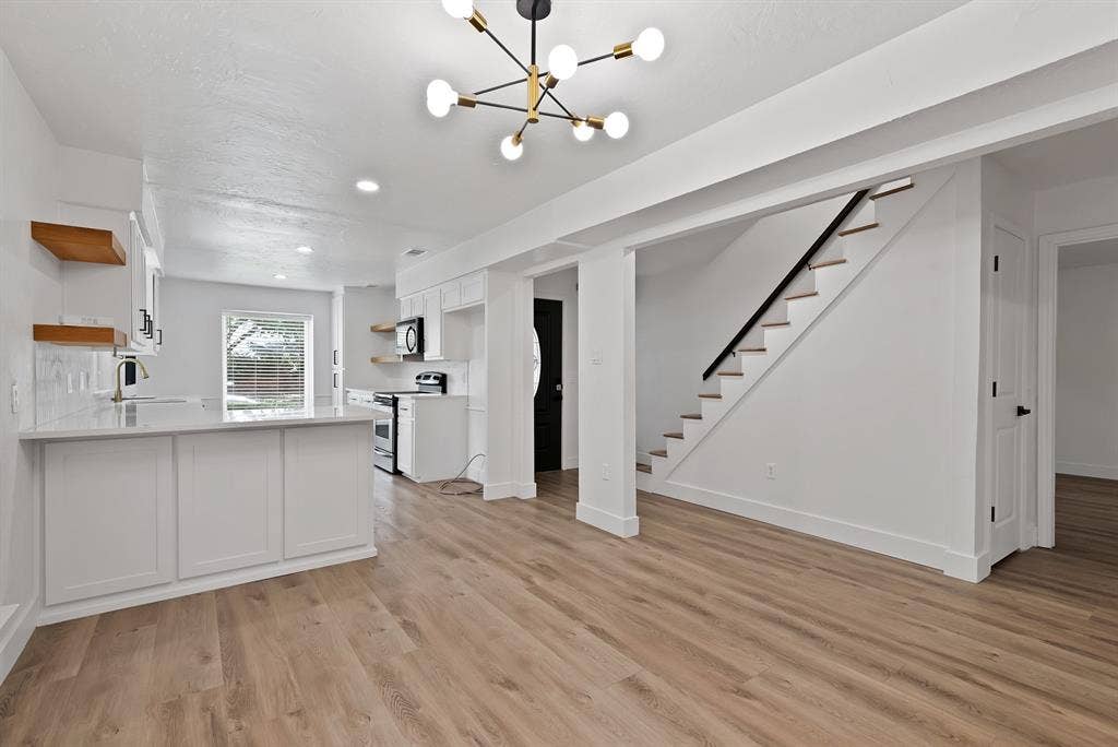 4021 San Mateo Drive, Plano, TX 75093 Open-concept main living space featuring wide-plank wood-finish flooring, a modern sputnik chandelier, and a white kitchen with shaker cabinetry