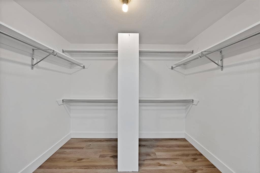4021 San Mateo Drive, Plano, TX 75093 Walk-in closet featuring wood-finish flooring, white baseboards, white walls, multiple hanging rods, and white shelving