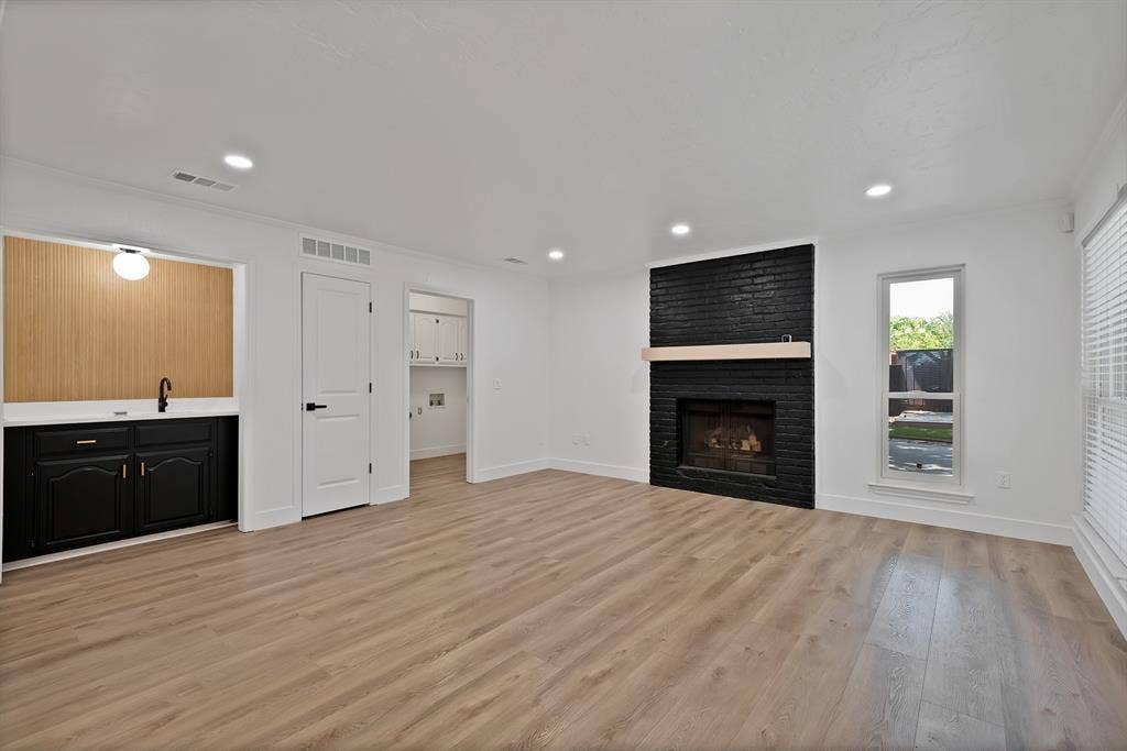 4021 San Mateo Drive, Plano, TX 75093 Living area featuring a black brick fireplace with a light wood mantel, wood-finish flooring, recessed lighting, and a built-in wet bar with black cabinetry and a light wood-paneled backsplash