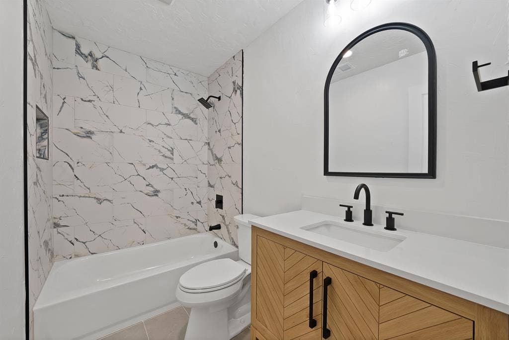 4021 San Mateo Drive, Plano, TX 75093 Modern bathroom featuring a white bathtub with marble-look tile surround, black shower fixtures, and a recessed shower niche