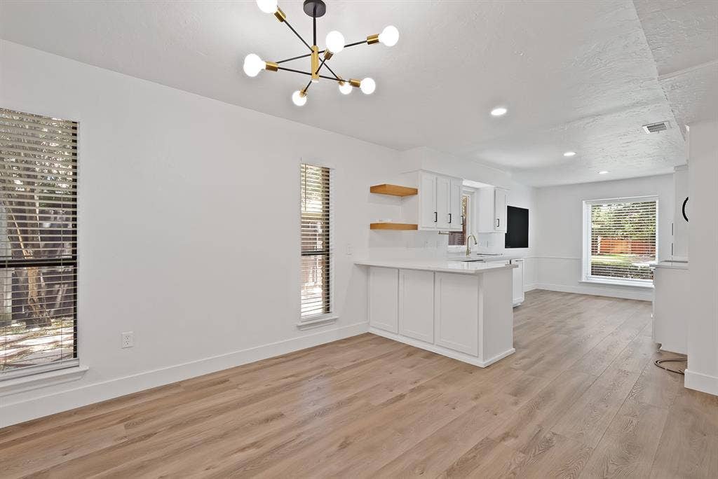 4021 San Mateo Drive, Plano, TX 75093 Open-concept living space featuring wood-finish flooring, a contemporary sputnik chandelier, multiple windows with horizontal blinds, and a built-in wet bar with white cabinetry and quartz countertop