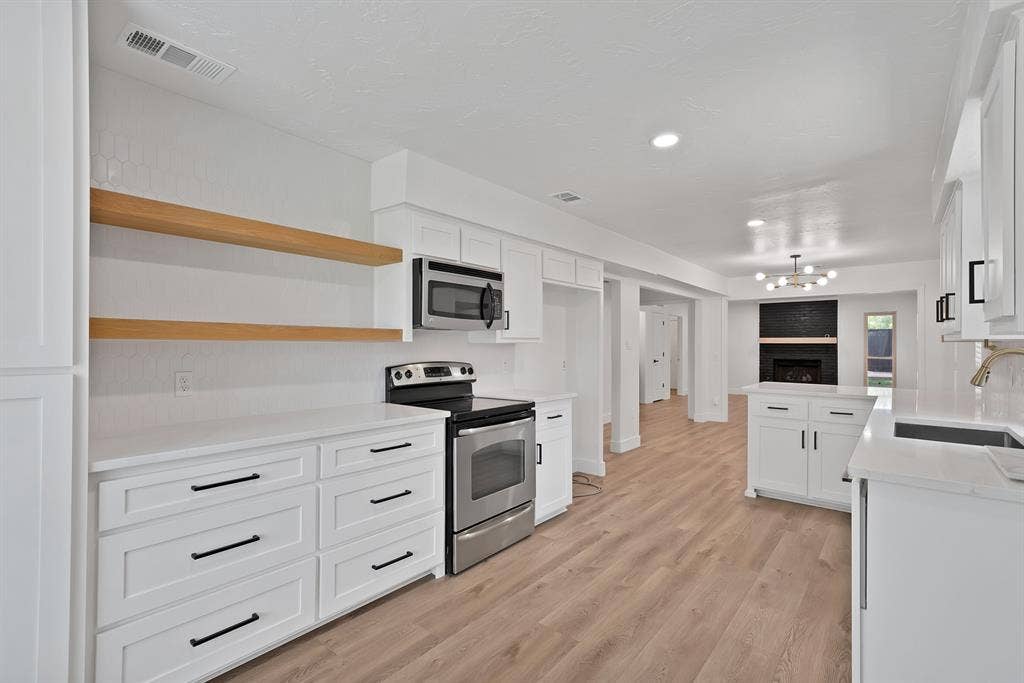 4021 San Mateo Drive, Plano, TX 75093 Open-concept kitchen featuring white cabinetry with black hardware, stainless steel appliances, wood-finish flooring, and white countertops