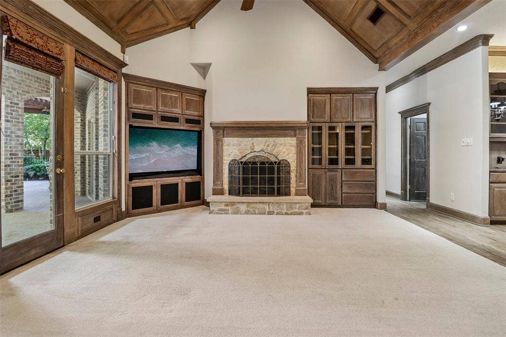 2600 Saratoga, McKinney, TX 75070 Vaulted wood-paneled ceiling, stone-surround fireplace with metal grate, built-in wooden media cabinetry, and French doors with transoms