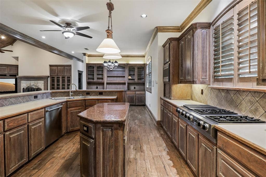 2600 Saratoga, McKinney, TX 75070 Spacious kitchen featuring extensive wood cabinetry, wood-finish flooring, a center island, stainless steel appliances, and built-in shelving