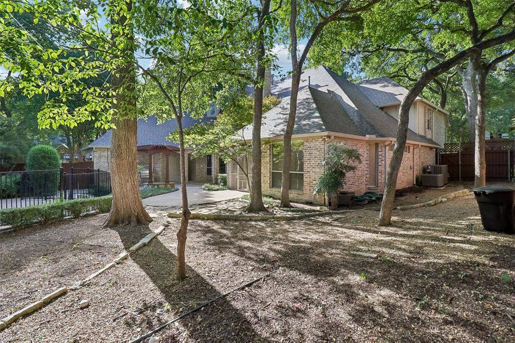 2600 Saratoga, McKinney, TX 75070 Brick exterior construction, multi-pitch shingle roof, mature trees, paved patio area, black iron fencing
