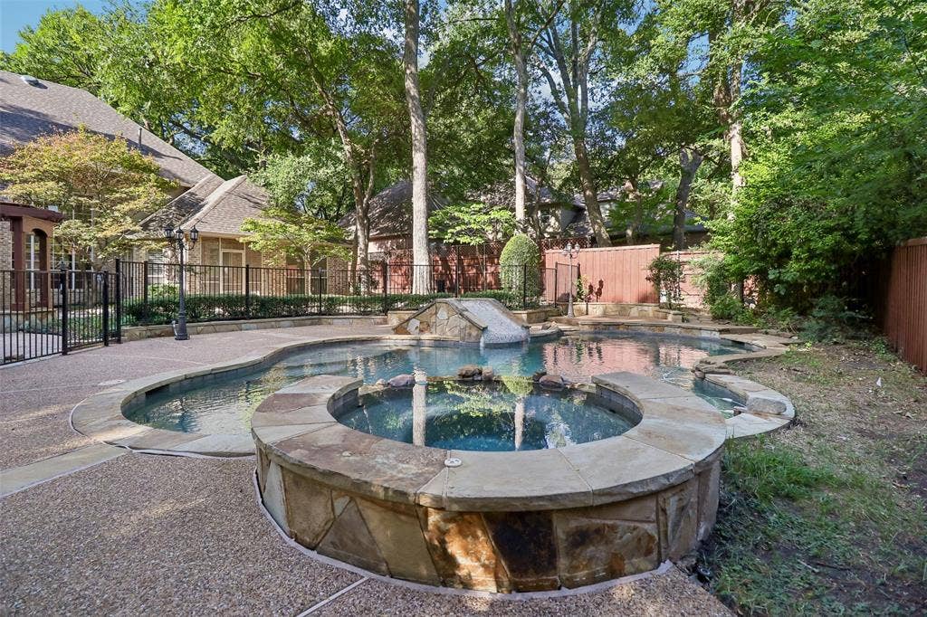 2600 Saratoga, McKinney, TX 75070 Multi-level swimming pool with a stone-clad spa, surrounded by aggregate concrete decking and a black metal fence