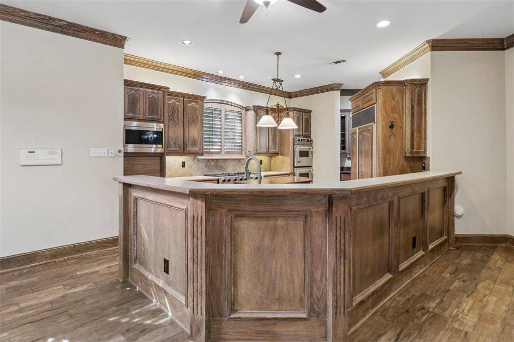 2600 Saratoga, McKinney, TX 75070 Kitchen featuring wood-finish flooring, a breakfast bar with a light-colored countertop, recessed lighting, and stainless steel appliances