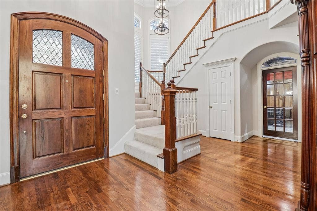 2600 Saratoga, McKinney, TX 75070 Hardwood flooring throughout, arched solid wood entry door with leaded glass, white painted wood staircase with carpeted treads, and recessed panel doors