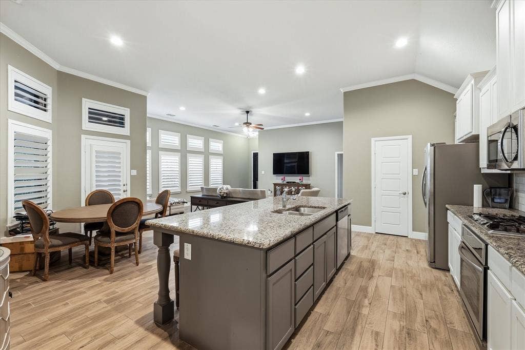 904 10th Street, Argyle, TX 76226 Spacious kitchen featuring a large island with a double sink, light wood-finish flooring, white cabinetry, stainless steel appliances, and granite countertops