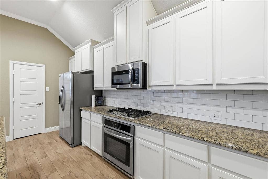 904 10th Street, Argyle, TX 76226 Kitchen featuring white shaker-style cabinetry, stainless steel appliances including a gas range and built-in microwave, stone countertops, a white subway tile backsplash, and wood-finish flooring