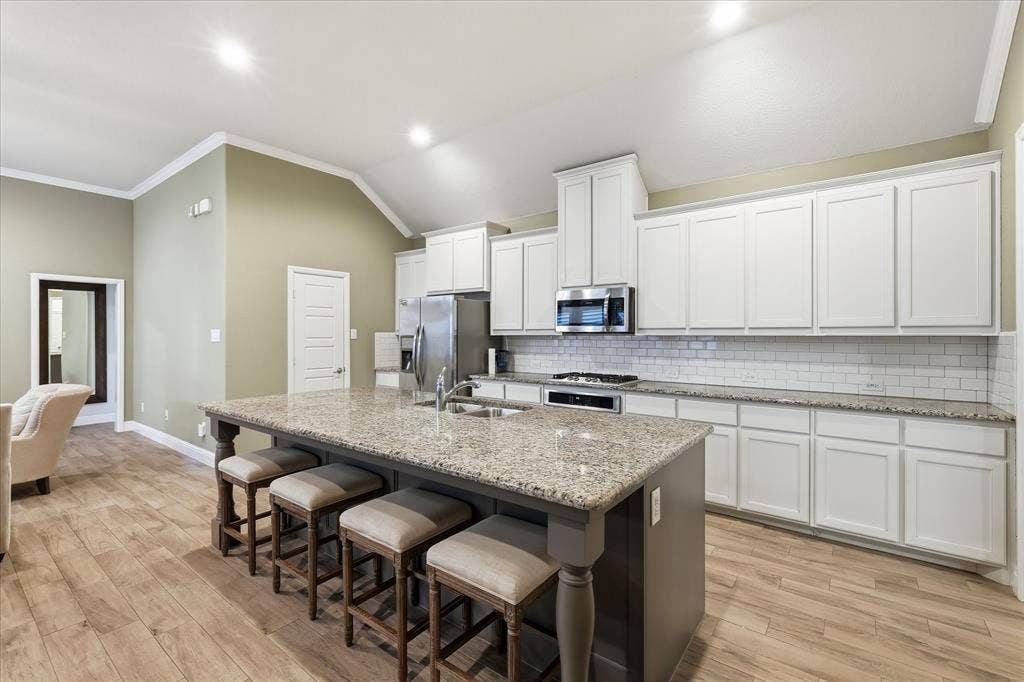 904 10th Street, Argyle, TX 76226 Kitchen featuring an expansive island with granite countertop, white shaker cabinetry, stainless steel appliances, white subway tile backsplash, and wood-finish flooring
