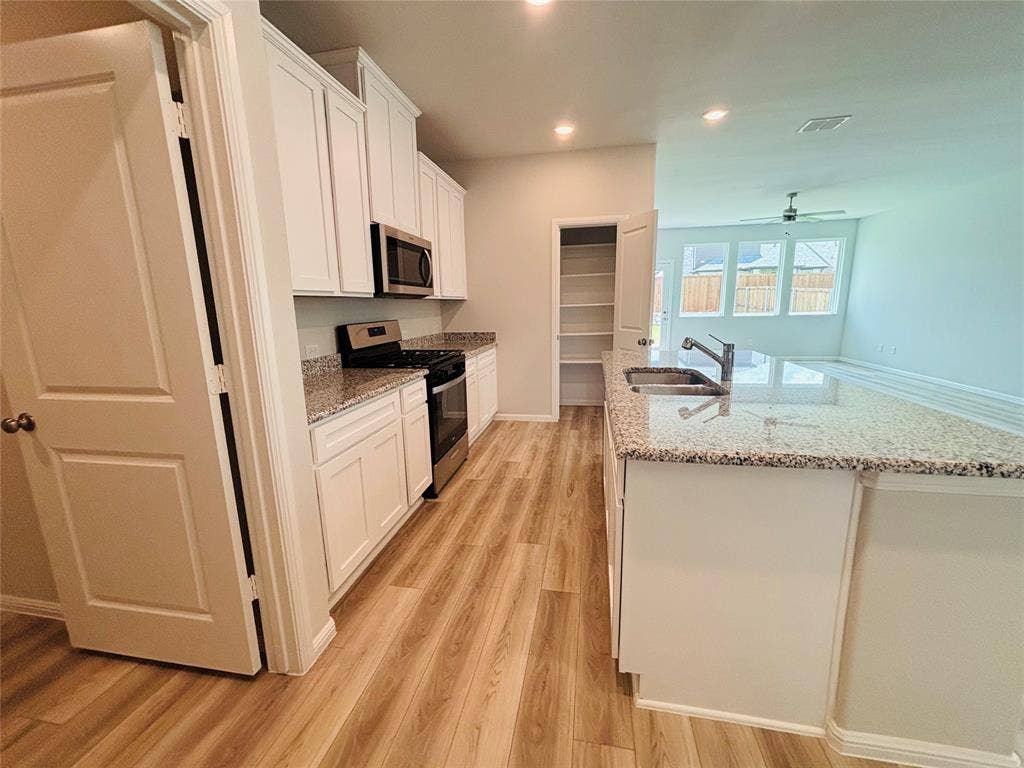 912 Santa Lucia Drive, Anna, TX 75409 Kitchen featuring appliances with stainless steel finishes, light wood finished floors, white cabinets, a kitchen island with sink, and a ceiling fan